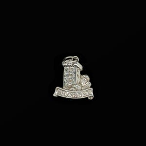 May include: A silver charm featuring a detailed depiction of a tower with a banner that reads "BLARNEY". The charm has a loop at the top for attachment and is set against a black background. The tower has multiple windows.