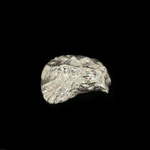 May include: A silver-colored ring with a textured, organic design. The ring has a rough, uneven surface, resembling a rock formation. The ring is set against a black background, highlighting its metallic sheen. The ring is a piece of jewelry.