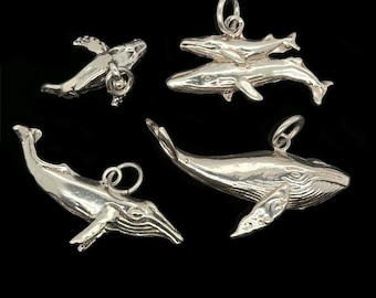 May include: Four silver whale charms with different designs. One charm shows a whale with its flippers extended. Another features two whales, one on top of the other. The other two charms show whales with detailed fin and body features. All charms have a small loop for attaching to a chain.