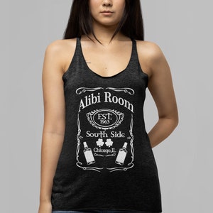 May include: A black tank top with a white graphic design that says "Alibi Room Est. 1963 South Side Chicago, IL" with two bottles of beer and three shamrocks.
