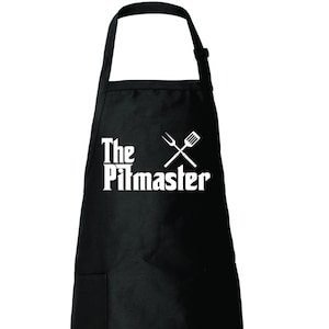 Peut inclure: Tablier noir avec une poche blanche et le texte "The Pitmaster" en gras avec un graphique de fourchette et spatule croisées.