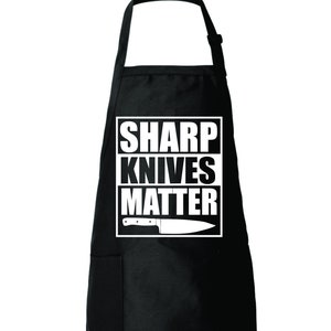 May include: Black kitchen apron with a white pocket and the text "SHARP KNIVES MATTER" with a knife graphic.