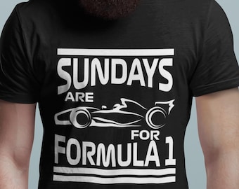 Può includere: T-shirt nero con la scritta bianca "SUNDAYS ARE FOR FORMULA 1". Il design include un'auto da corsa di Formula 1 stilizzata. La maglietta è a girocollo.