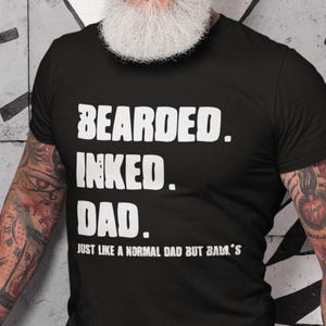 May include: A black t-shirt with white text that reads "Bearded. Inked. Dad. Just like a normal dad but BAM's". The person wearing the shirt has a long white beard and tattoos on their arms.