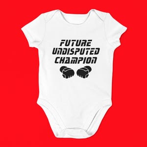 May include: White baby onesie with the text "FUTURE UNDISPUTED CHAMPION" in black. The onesie features a pair of black boxing gloves below the text. The background is a solid red.
