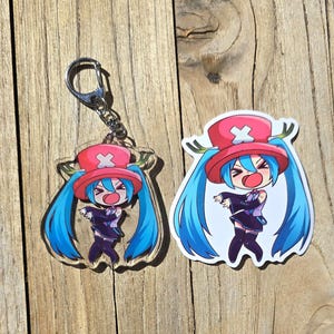 May include: A clear acrylic keychain and sticker featuring a cartoon character with blue hair, a red hat, and a black outfit. The keychain has a silver metal ring.