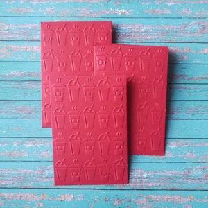 May include: Three red cards with a repeating pattern of coffee cups with steam coming from the top. The cards are stacked on top of each other.