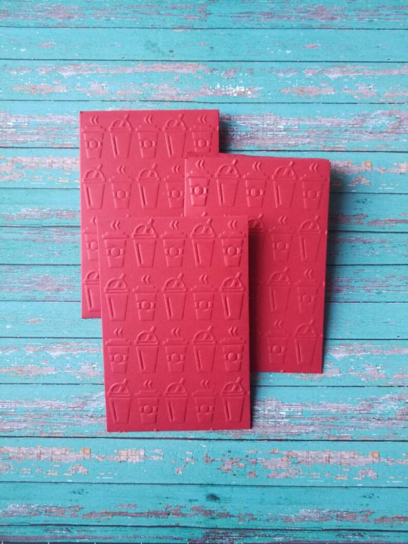 May include: Three red cards with a repeating pattern of coffee cups with steam coming from the top. The cards are stacked on top of each other.