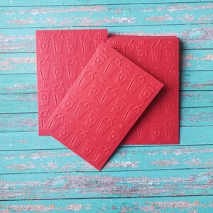 May include: Three red paper squares with a repeating pattern of a coffee cup with steam coming from the top. The squares are stacked on top of each other.