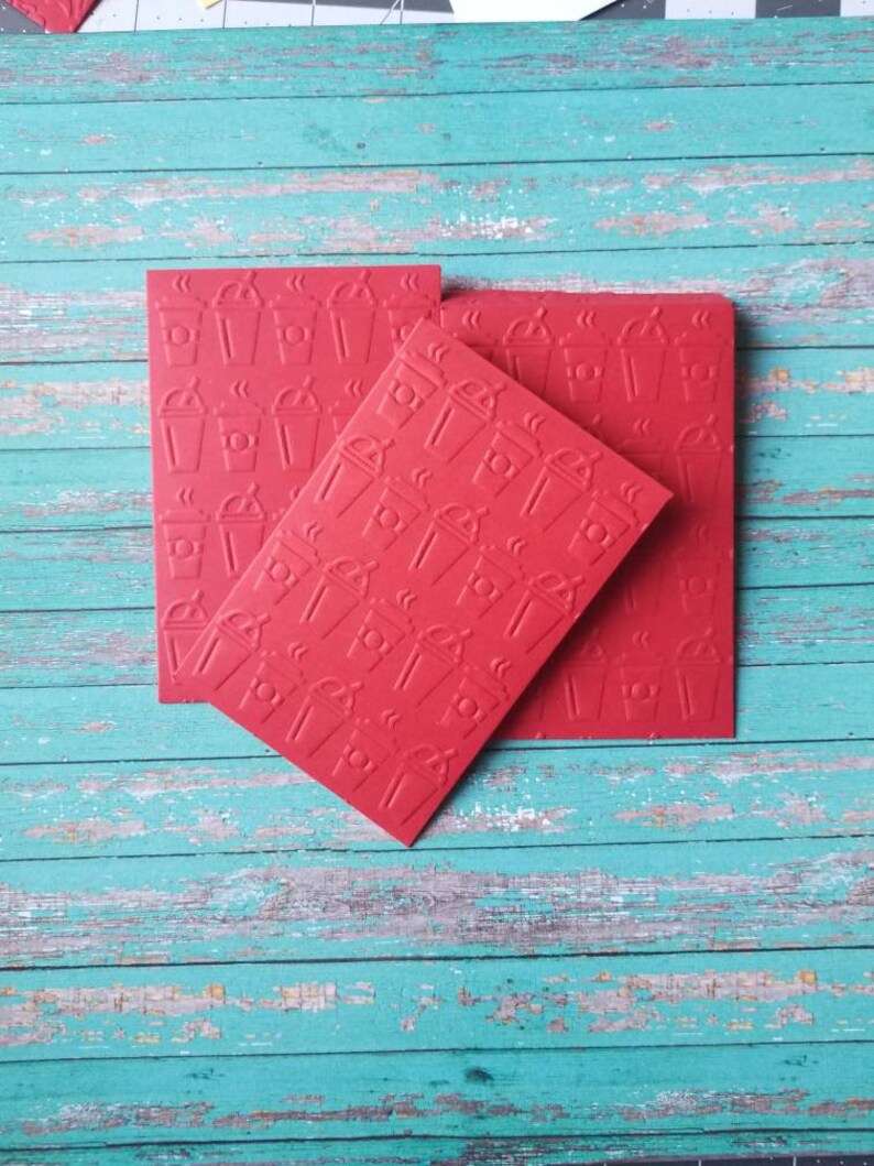 May include: Three red paper squares with a repeating pattern of a coffee cup with steam coming from the top. The squares are stacked on top of each other.