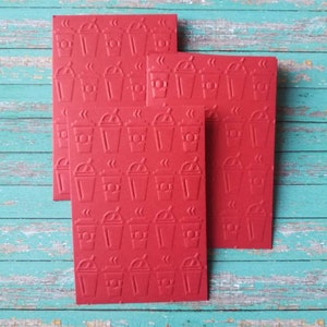 May include: Four red cards with a repeating pattern of coffee cups. The cups are embossed and have steam coming from the top.