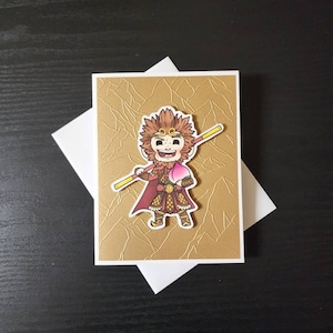 May include: A gold card with a textured surface. A cartoon illustration of a monkey holding a peach and a staff is on the card.
