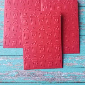 May include: Four red cards with a repeating pattern of a coffee cup with steam coming from the top. The cards are stacked on top of each other.