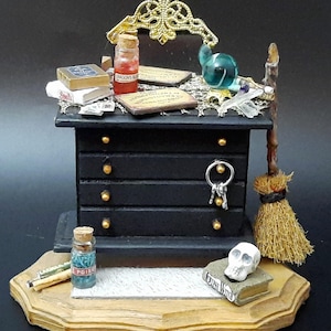 May include: Miniature black cabinet with gold accents, holding keys and topped with potion bottles, books, and a decorative gold filigree. A small broom and skull sit nearby, creating a whimsical, fantasy-themed display.