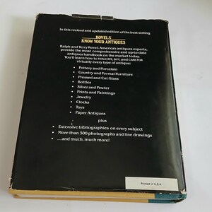 May include: A vintage hardcover book titled "Know Your Antiques" by Ralph and Terry Kovel. The black cover features white text listing antique categories like pottery, furniture, and jewelry. The book is printed in the USA.