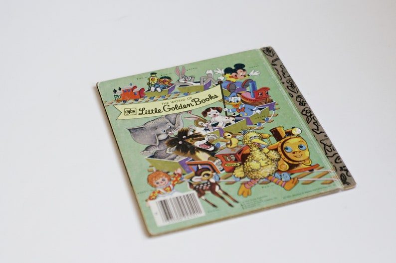 Op de afbeelding: De achterkant van een klein gouden boekje met de titel "De wereld van kleine gouden boekjes". De omslag toont een kleurrijke illustratie van verschillende personages, waaronder een olifant, een leeuw, een vogel en een trein. Het boek is groen met een gouden rug.