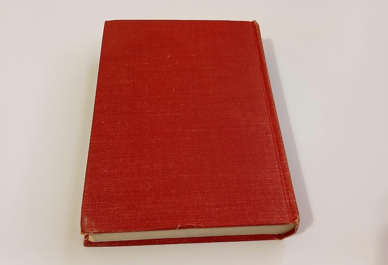 May include: A hardcover book with a red cover. The book is closed and slightly angled, showing the spine and edges of the pages. The cover has a textured appearance.