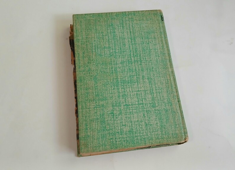 May include: An antique book with a textured green cover. The cover has a subtle crosshatch pattern. The spine is worn, revealing the aged pages. The book is slightly angled, showcasing its well-loved condition.