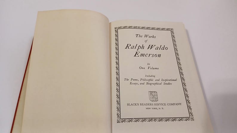 May include: An open book with the title page of "The Works of Ralph Waldo Emerson" in black text. The page includes the text "in One Volume" and "Including The Poems, Philosophic and Inspirational Essays, and Biographical Studies."