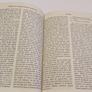 May include: An open book with red covers, displaying text from "Works of Ralph Waldo Emerson" and "Essays." The pages are yellowed, suggesting age. The text is in black, with a clear font. The book is on a white surface.