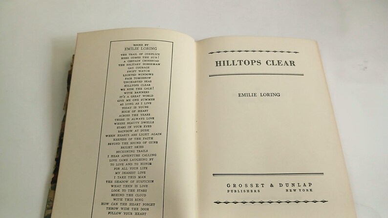 May include: Open book titled "Hilltops Clear" by Emilie Loring. The left page lists poems by the author. The right page displays the title and author's name. The publisher's name and location are at the bottom.