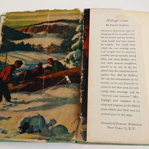 May include: Open vintage book titled "Hilltop Star" by Emilie Loring. The cover art depicts two men in a snowy landscape. The book's pages are yellowed with age, and the text is visible on the right page.