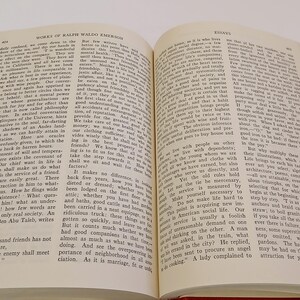 May include: Open book with text, titled "Works of Ralph Waldo Emerson" and "Essays". The pages are cream-colored with black text. The book has a red cover and is open to a double-page spread.