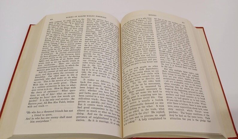May include: Open book with text, titled "Works of Ralph Waldo Emerson" and "Essays". The pages are cream-colored with black text. The book has a red cover and is open to a double-page spread.