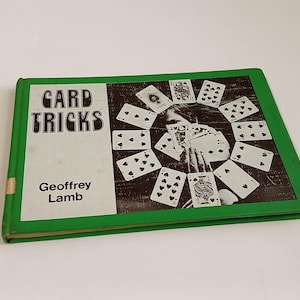 May include: A vintage book titled "Card Tricks" by Geoffrey Lamb. The cover features a green border and a black and white illustration of a magician surrounded by playing cards. The book is on a white surface.