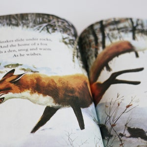 Op de afbeelding: Een open boek met een illustratie van een rode vos die door een besneeuwd bos loopt. De tekst op de pagina luidt: "Slangen glijden onder rotsen, En het huis van een vos Is een hol, knus en warm Zoals hij het wenst."