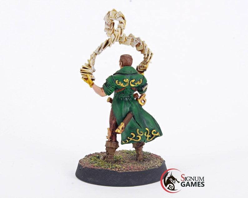 May include: A painted miniature figure of a wizard holding a swirling stack of papers in their left hand. The figure is wearing a green coat with gold accents and is standing on a round base.