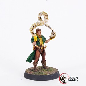May include: A painted miniature figurine of a person wearing a green coat and brown pants, holding a swirling stack of cards above their head. The figurine is standing on a round base with green grass and brown dirt.