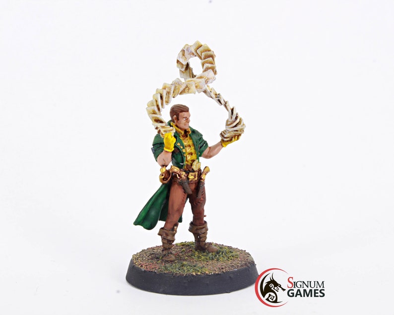 May include: A painted miniature figurine of a person wearing a green coat and brown pants, holding a swirling stack of cards above their head. The figurine is standing on a round base with green grass and brown dirt.