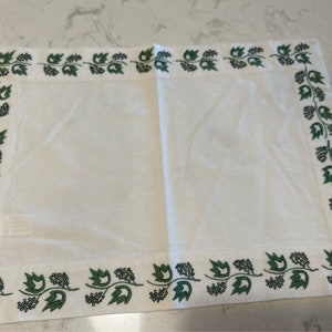 May include: White linen table runner with a green embroidered border of leaves and vines.