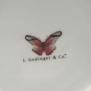 May include: White ceramic dish with a butterfly design in shades of red, pink, and black. The text "I. Godinger & Co." is printed below the butterfly. The dish has a slightly scalloped edge.