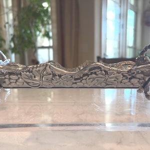 May include: A white ceramic mug with a black handle and the text "But First, Coffee" in a black, handwritten-style font. The mug is on a white surface.