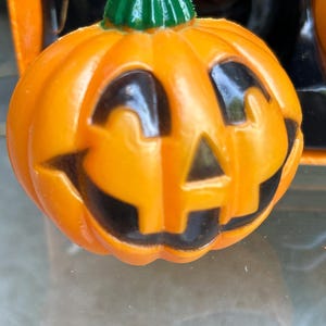 May include: Orange plastic Halloween jack-o'-lantern light with a smiling face and a green stem. The light has black painted features and is designed to be part of a string of lights for seasonal decor.