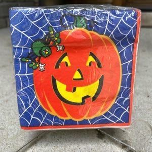 May include: A blue and orange Halloween themed paper napkin with a jack-o-lantern face and a green spider with black legs on a web.