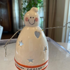 May include: White ceramic ghost figurine with a smiling face, pink cheeks, and a heart-shaped cutout. The ghost has wire arms and a base with the text "Gonna Getcha..." in orange.