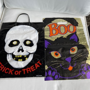 May include: Two Halloween trick or treat bags. One bag features a black and white skull with the text "Trick or Treat" and "Made in China". The other bag features a black cat with orange eyes and a purple tongue with the text "BOO" in orange letters.