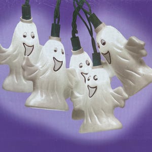 May include: A string of Halloween lights featuring smiling white ghost-shaped bulbs. Each ghost has a black mouth and eyes, with green wiring. The lights are set against a purple background, with the words "HAPPY GHOSTS" visible.