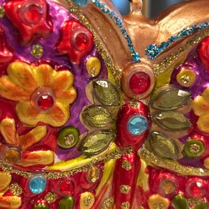 May include: A colorful glass butterfly ornament with red, yellow, green, and blue accents. The butterfly has a glittery finish and is decorated with rhinestones.