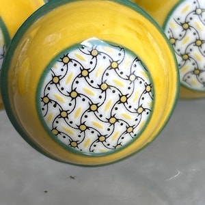 May include: Yellow ceramic cabinet knobs with a green border and a patterned center. The center design features a white background with black dots and yellow starburst shapes. Decorative hardware for furniture.