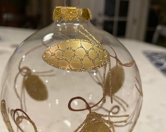Hand painted clear glass ornament with gold, glitter pinecones. Hand blown glass. Unknown manufacturer.