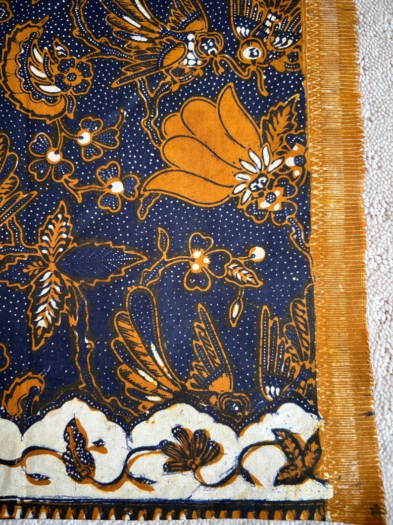 K&ouml;nnte beinhalten: Ein blauer und orangefarbener Stoff mit einem traditionellen indonesischen Batik-Muster. Das Muster zeigt V&ouml;gel, Blumen und Bl&auml;tter.