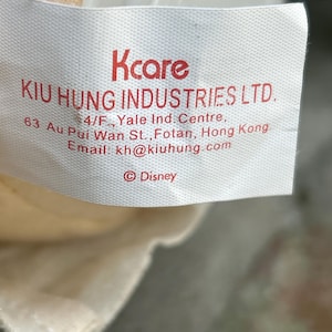 May include: A white tag with red text that reads "Kcare" and "KIU HUNG INDUSTRIES LTD." Additional text includes an address and email. The Disney logo is at the bottom.