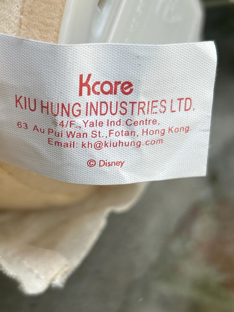 May include: A white tag with red text that reads "Kcare" and "KIU HUNG INDUSTRIES LTD." Additional text includes an address and email. The Disney logo is at the bottom.