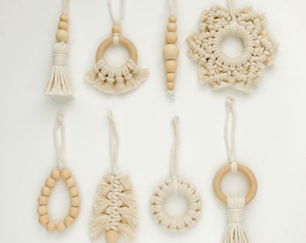 Könnte beinhalten: Acht handgefertigte Makramee-Anhänger mit Holzperlen und Ringen. Die Anhänger sind in Form einer Quaste, eines Rings, einer Schneeflocke, einer Perlenkette, eines Baumes, eines Kreises und einer Quaste mit einem Ring.
