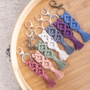 Op de afbeelding: Een set van acht kleurrijke macramé sleutelhangers met kwastjes. De sleutelhangers zijn gemaakt van verschillende gekleurde garens en zijn bevestigd aan zilveren sleutelringen.