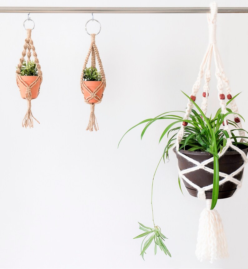 May include: Three macrame plant hangers with potted plants. The hangers are made of natural fibre rope and have wooden beads. The plants are green and leafy.